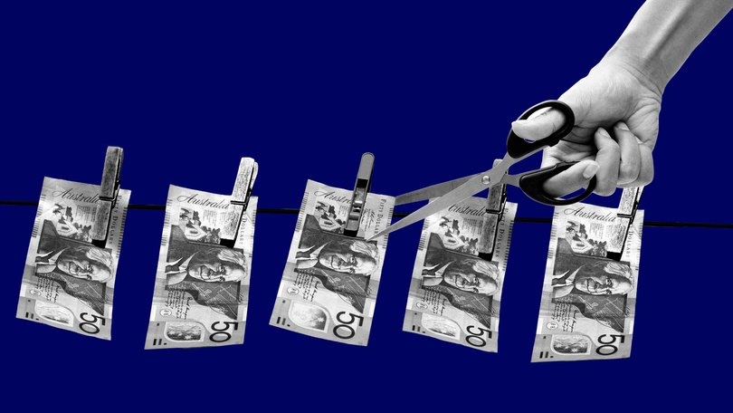 A hand holding scissors cutting a line of Australian 50 dollar bills hanging from clothespins against a blue background.