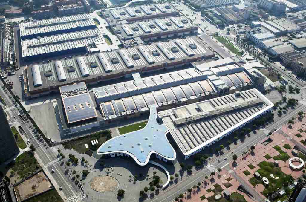 Aerial view of a large modern building complex featuring a unique architectural design resembling a whale, surrounded by multiple warehouse structures and landscaped areas.
