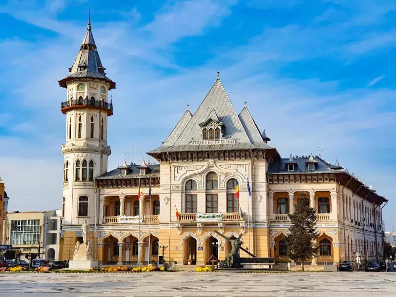 A historic Romania city hall building featuring a large tower and intricate architectural details, surrounded by a clear blue sky.