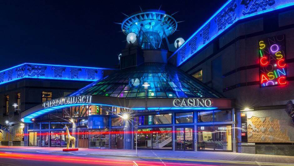 Exterior of the Christchurch Casino at night, featuring vibrant blue lighting and a neon sign.